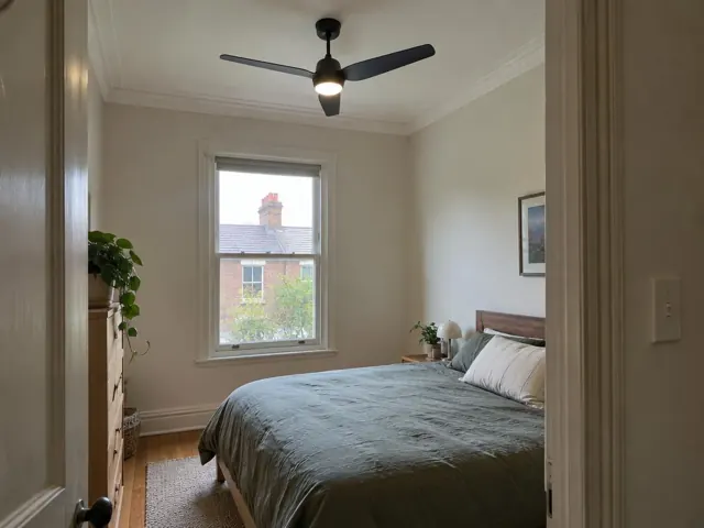 Bedroom with black ceiling fan, window, bed and light walls in Lilyfield