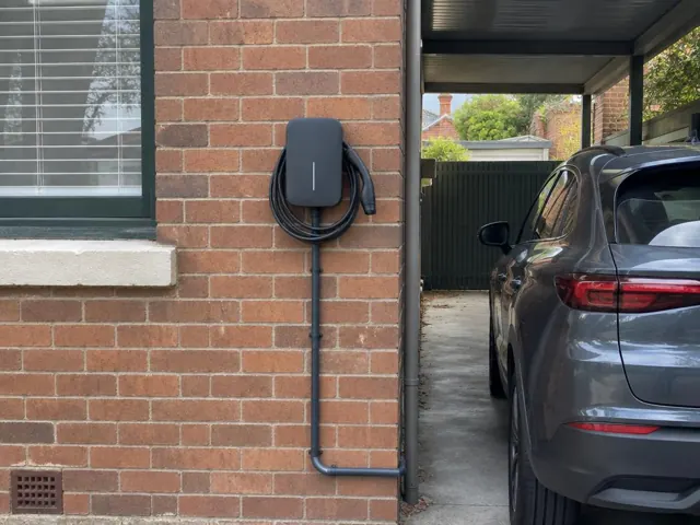 Wall-mounted EV charger with coiled cable on a brick exterior wall beside a driveway in Leichhardt